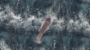 Supply chain resilience: aerial view of a container ship navigating rough, foamy seas during a global disruption.